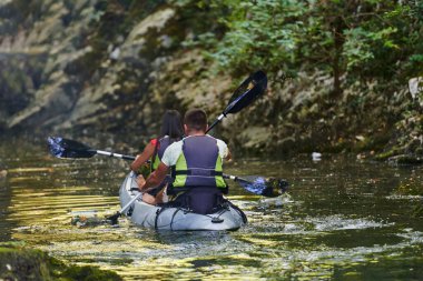 Genç bir çift orman yeşiliyle çevrili güzel bir nehrin ortasında kayak gezintisinin tadını çıkarıyor.. 