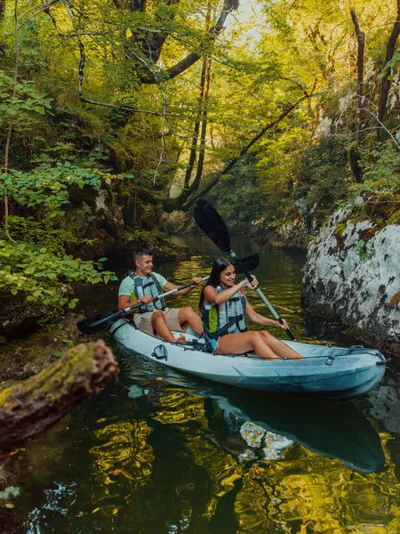 森の緑に囲まれた美しい川の真ん中で牧歌的なカヤックに乗る若いカップル — ストック写真