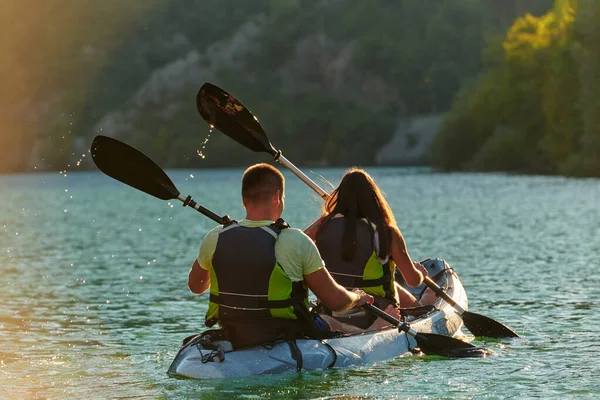 在日落时分 一对年轻夫妇在一条美丽的河流中央享受着田园诗般的独木舟之旅 河流周围环绕着茂密的绿叶 — 图库照片
