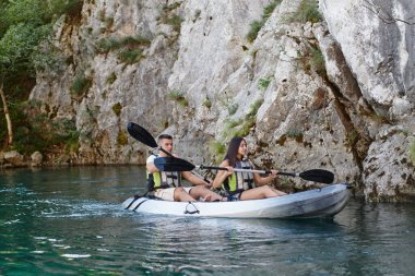 Genç bir çift orman yeşiliyle çevrili güzel bir nehrin ortasında kayak gezintisinin tadını çıkarıyor.. 