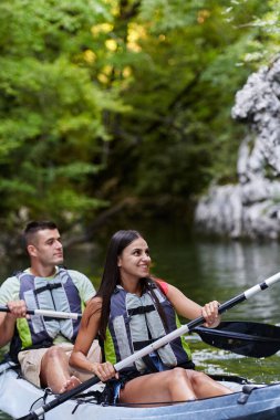 Genç bir çift orman yeşiliyle çevrili güzel bir nehrin ortasında kayak gezintisinin tadını çıkarıyor.. 