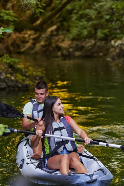 森の緑に囲まれた美しい川の真ん中で牧歌的なカヤックに乗る若いカップル — ストック写真