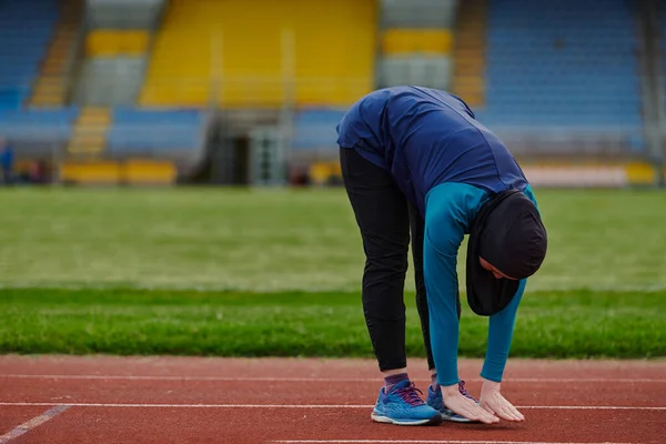 A Muslim woman in a burqa, an Islamic sports outfit, is doing body exercises, stretching her neck, legs and back after a hard training session on the marathon course