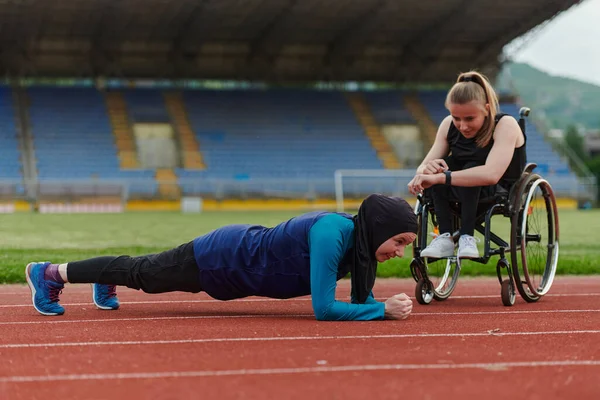 stock image Two strong and inspiring women, one a Muslim wearing a burka and the other in a wheelchair stretching and preparing their bodies for a marathon race on the track.