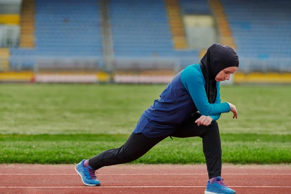 A Muslim woman in a burqa, an Islamic sports outfit, is doing body exercises, stretching her neck, legs and back after a hard training session on the marathon course