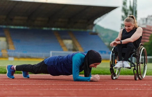 stock image Two strong and inspiring women, one a Muslim wearing a burka and the other in a wheelchair stretching and preparing their bodies for a marathon race on the track.