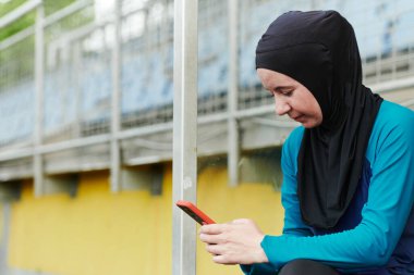Yeşil doğa parkında tesettürlü, koyu renk elbiseli, cep telefonu sohbeti yapan Müslüman spor kadın.. 