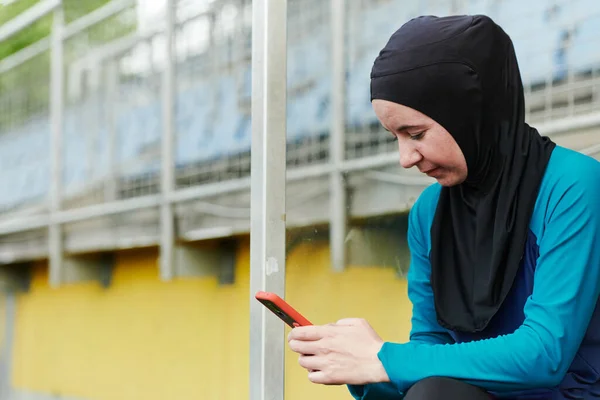 携帯電話のチャットを使用して緑の自然公園でヒジャーブと暗い服を屋外で身に着けているイスラム教徒のスポーツフィットネス女性 — ストック写真
