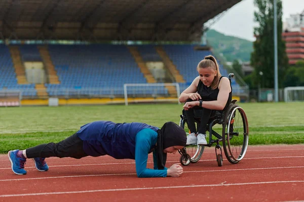 stock image Two strong and inspiring women, one a Muslim wearing a burka and the other in a wheelchair stretching and preparing their bodies for a marathon race on the track.