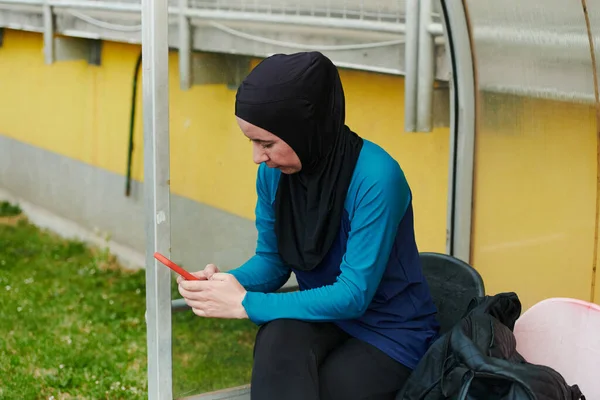 在绿色自然公园里 穆斯林运动健美女子身穿头巾 身穿深色衣服 用手机聊天 — 图库照片