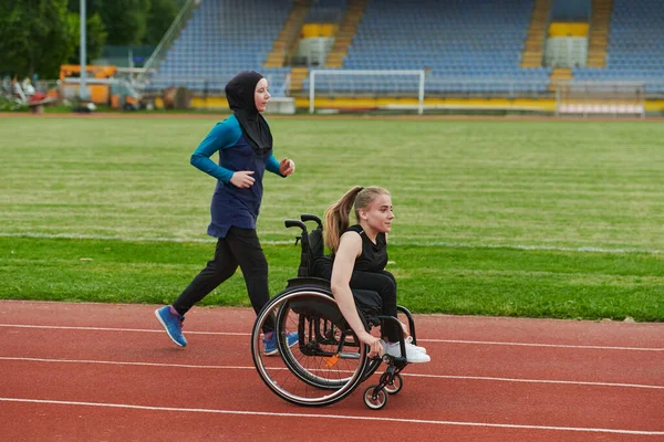 マラソンコースの車椅子の女性と一緒に走るブルカのイスラム教徒の女性 将来の競技会の準備 — ストック写真