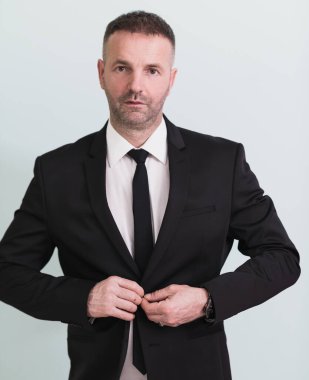 Başarıya alışığım. Kendine güvenen genç işadamı gri arka planda dikilirken ceketini ayarlıyor ve gözünü kaçırıyor. Yüksek kalite fotoğraf