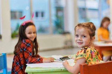 Bir kreşteki resim dersinde yaratıcı çocuklar ya da ilkokul sınıfında bayan öğretmenle resim çizen çocuklar.