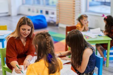 Bir kreşteki resim dersinde yaratıcı çocuklar ya da ilkokul sınıfında bayan öğretmenle resim çizen çocuklar.