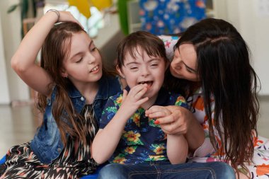 Modern bir anaokulunda bir kız ve bir kadın Down sendromlu bir çocuğa sarılıyor. Yüksek kalite fotoğraf