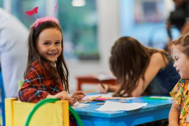 Bir kreşteki resim dersinde yaratıcı çocuklar ya da ilkokul sınıfında bayan öğretmenle resim çizen çocuklar.