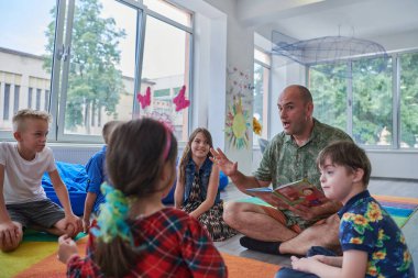 İlkokulda ya da anaokulunda okuma süresi, ilkokulda ya da anaokulunda çocuklara kitap okuyan bir öğretmen. Okul öncesi eğitim kavramı. Seçici odak.