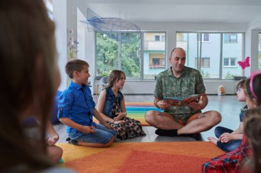 İlkokulda ya da anaokulunda okuma süresi, ilkokulda ya da anaokulunda çocuklara kitap okuyan bir öğretmen. Okul öncesi eğitim kavramı. Seçici odak.