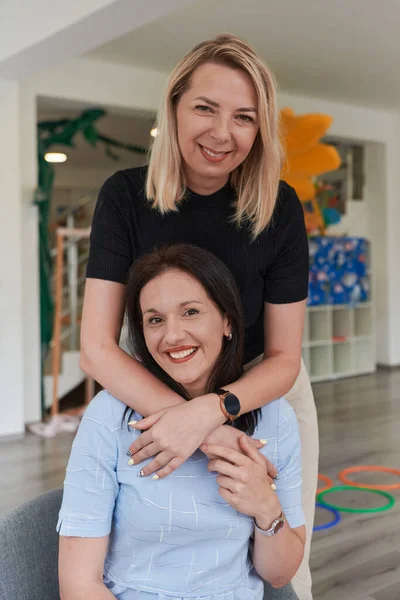 Δύο Γυναίκες Μοιράζονται Μια Εγκάρδια Αγκαλιά Ενώ Ένα Νηπιαγωγείο Αναδεικνύοντας — Φωτογραφία Αρχείου