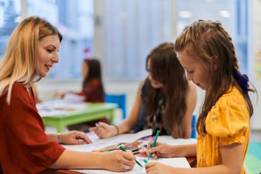 Bir kreşteki resim dersinde yaratıcı çocuklar ya da ilkokul sınıfında bayan öğretmenle resim çizen çocuklar.