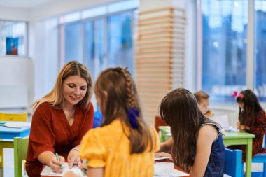 Bir kreşteki resim dersinde yaratıcı çocuklar ya da ilkokul sınıfında bayan öğretmenle resim çizen çocuklar.