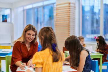 Bir kreşteki resim dersinde yaratıcı çocuklar ya da ilkokul sınıfında bayan öğretmenle resim çizen çocuklar.