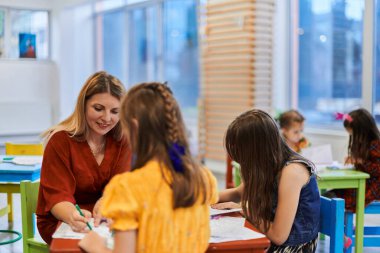 Bir kreşteki resim dersinde yaratıcı çocuklar ya da ilkokul sınıfında bayan öğretmenle resim çizen çocuklar.