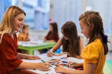 Bir kreşteki resim dersinde yaratıcı çocuklar ya da ilkokul sınıfında bayan öğretmenle resim çizen çocuklar.