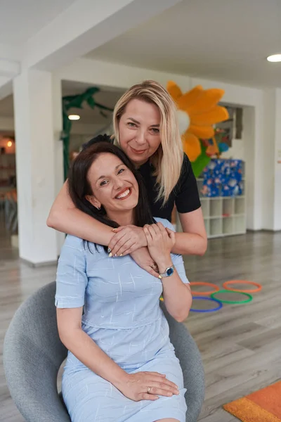Dos Mujeres Comparten Abrazo Sincero Mientras Están Preescolar Mostrando Ambiente —  Fotos de Stock