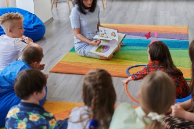 İlkokulda ya da anaokulunda okuma süresi, ilkokulda ya da anaokulunda çocuklara kitap okuyan bir öğretmen. Okul öncesi eğitim kavramı. Seçici odak.