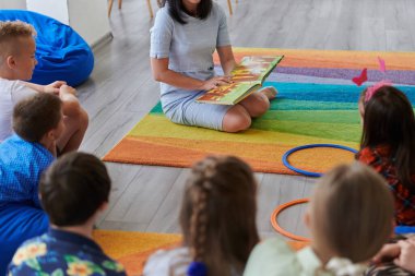 İlkokulda ya da anaokulunda okuma süresi, ilkokulda ya da anaokulunda çocuklara kitap okuyan bir öğretmen. Okul öncesi eğitim kavramı. Seçici odak.
