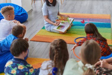 İlkokulda ya da anaokulunda okuma süresi, ilkokulda ya da anaokulunda çocuklara kitap okuyan bir öğretmen. Okul öncesi eğitim kavramı. Seçici odak.