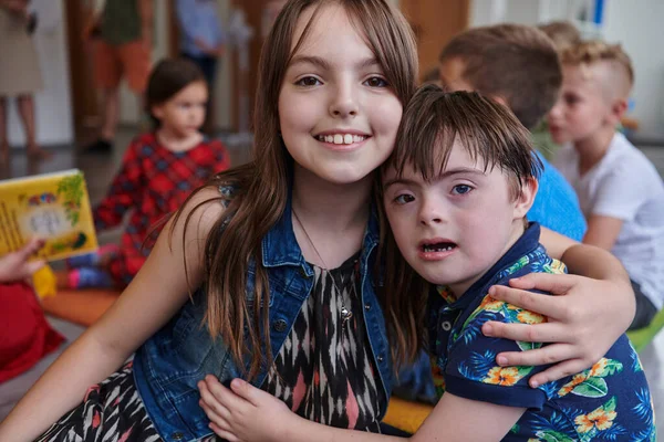 一个女孩和一个患有唐氏综合症的男孩抱着胳膊在幼儿园里呆在一起 — 图库照片