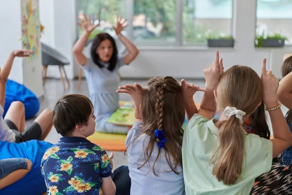 Szczęśliwa Nauczycielka Siedząca Grająca Karty Grupą Małych Uczniów — Zdjęcie stockowe