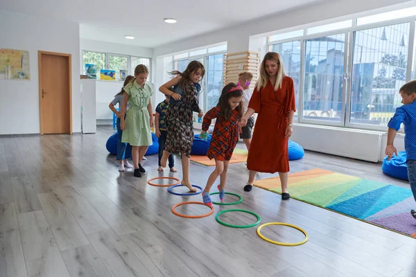 Små Förskolebarn Med Kvinnlig Lärare Golvet Inomhus Klassrummet Motionerar Hoppa Stockfoto