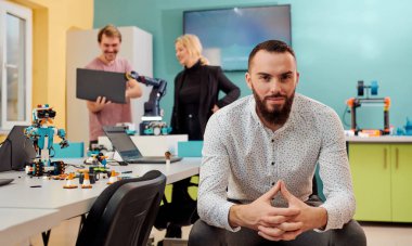 Arka plandaki meslektaşları yeni, ileri teknoloji robot icatlarını test ederken bir adam robot laboratuarında oturuyor.