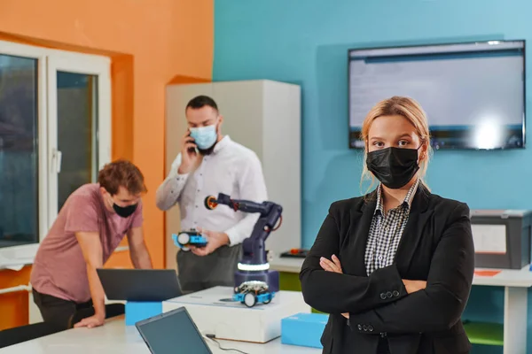 一位戴着防护面具的女士站在实验室里 她的同事们正在后台测试一项新的机器人发明 — 图库照片