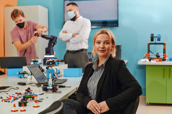 A woman sitting in a laboratory while her colleagues test a new robotic invention in the background. 