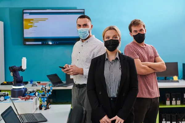 一组同事站在机器人实验室里 双手交叉 戴着防护面具 象征着他们的团队精神以及对技术创新和科学研究的承诺 — 图库照片