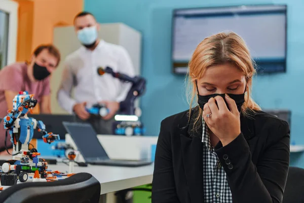 一位戴着防护面具的女士站在实验室里 她的同事们正在后台测试一项新的机器人发明 — 图库照片