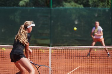 Genç kızlar güneşli bir günde canlı bir tenis maçında modern bir tenis kortunda yeteneklerini ve heveslerini gösteriyorlar.
