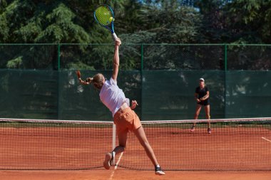 Genç kızlar güneşli bir günde canlı bir tenis maçında modern bir tenis kortunda yeteneklerini ve heveslerini gösteriyorlar.