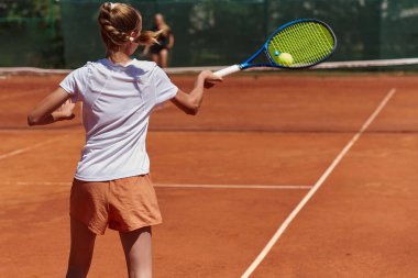 Güneşli bir günde tenis kortunun modern estetiğiyle çevrili profesyonel tenis yetenekleri sergileyen genç bir kız.