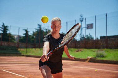 Güneşli bir günde tenis kortunun modern estetiğiyle çevrili profesyonel tenis yetenekleri sergileyen genç bir kız.