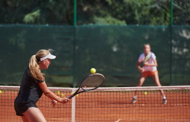 Genç kızlar güneşli bir günde canlı bir tenis maçında modern bir tenis kortunda yeteneklerini ve heveslerini gösteriyorlar.