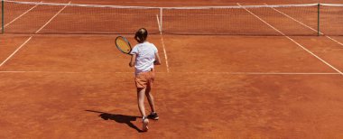 Güneşli bir günde tenis kortunun modern estetiğiyle çevrili profesyonel tenis yetenekleri sergileyen genç bir kız.