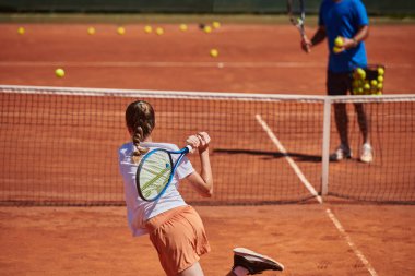 Profesyonel bir tenisçi ve onun koçu tenis kortunda güneşli bir günde antrenman yapıyorlar. Profesyonel bir tenisçinin antrenmanı ve hazırlığı.