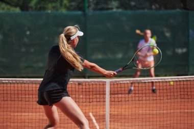 Genç kızlar güneşli bir günde canlı bir tenis maçında modern bir tenis kortunda yeteneklerini ve heveslerini gösteriyorlar.