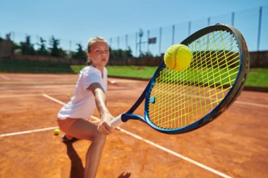 Güneşli bir günde tenis kortunun modern estetiğiyle çevrili profesyonel tenis yeteneklerini sergileyen genç bir kızın yakın plan fotoğrafı.