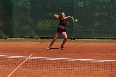 Güneşli bir günde tenis kortunun modern estetiğiyle çevrili profesyonel tenis yetenekleri sergileyen genç bir kız.
